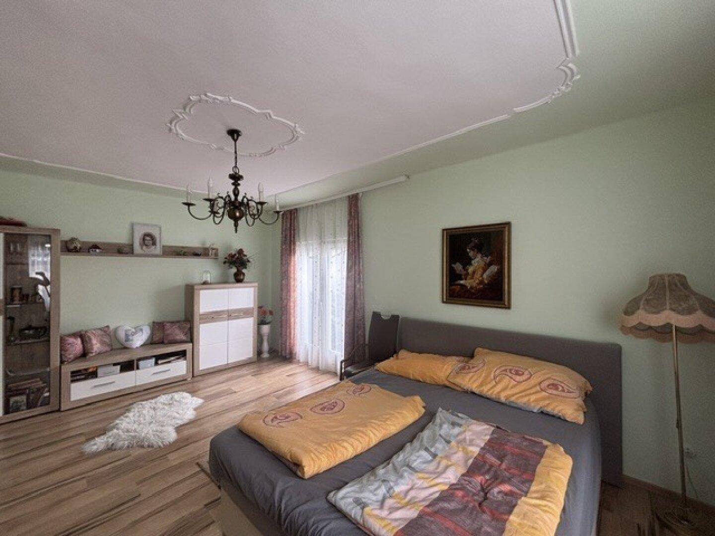 Geräumiges Schlafzimmer mit Holzboden, Doppelbett und klassischer Deckenverzierung.