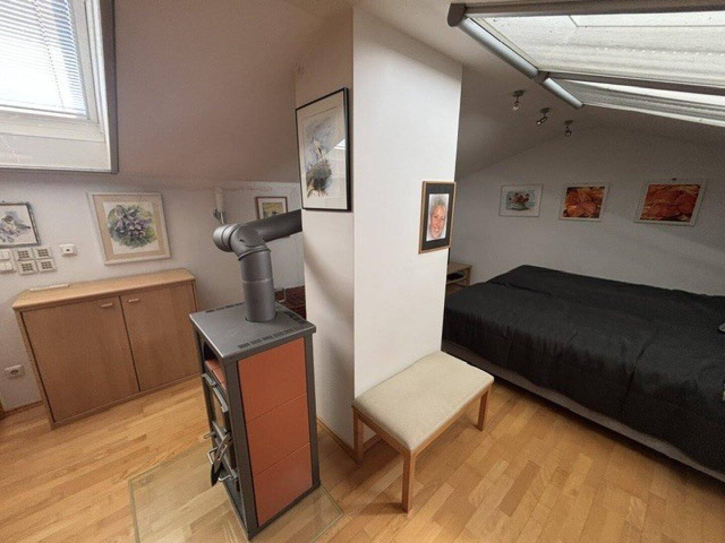 Gemütlicher Schlafbereich im Dachgeschoss mit Kaminofen und Holzboden unter Dachfenstern.