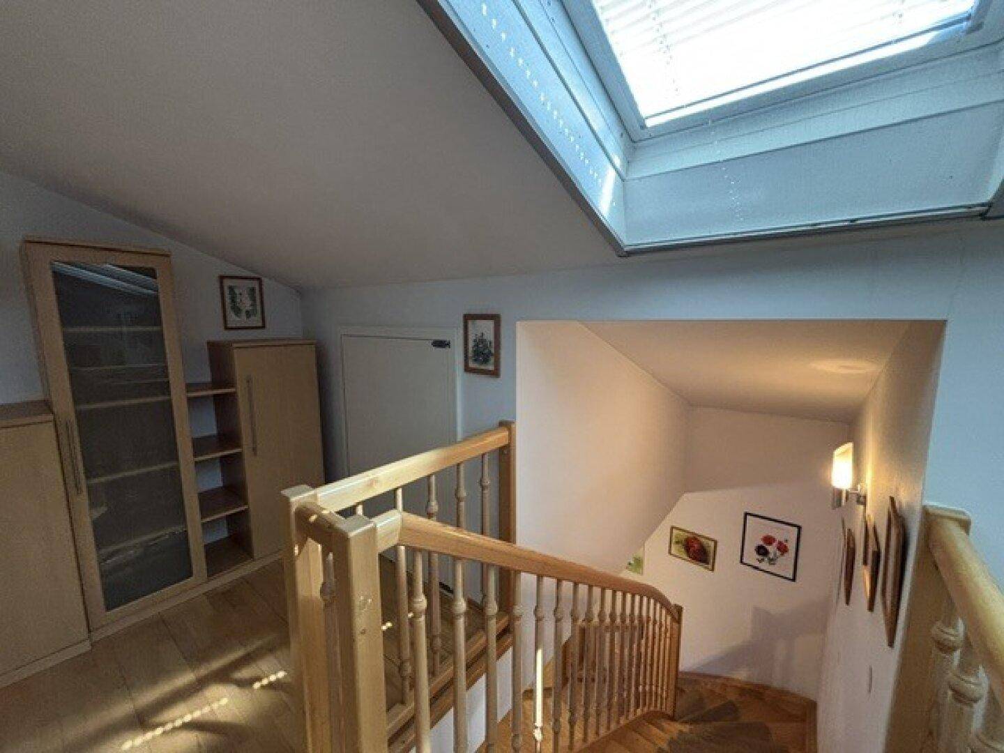 Helle Holztreppe führt zum Dachgeschoss, beleuchtet durch ein großes Dachfenster.