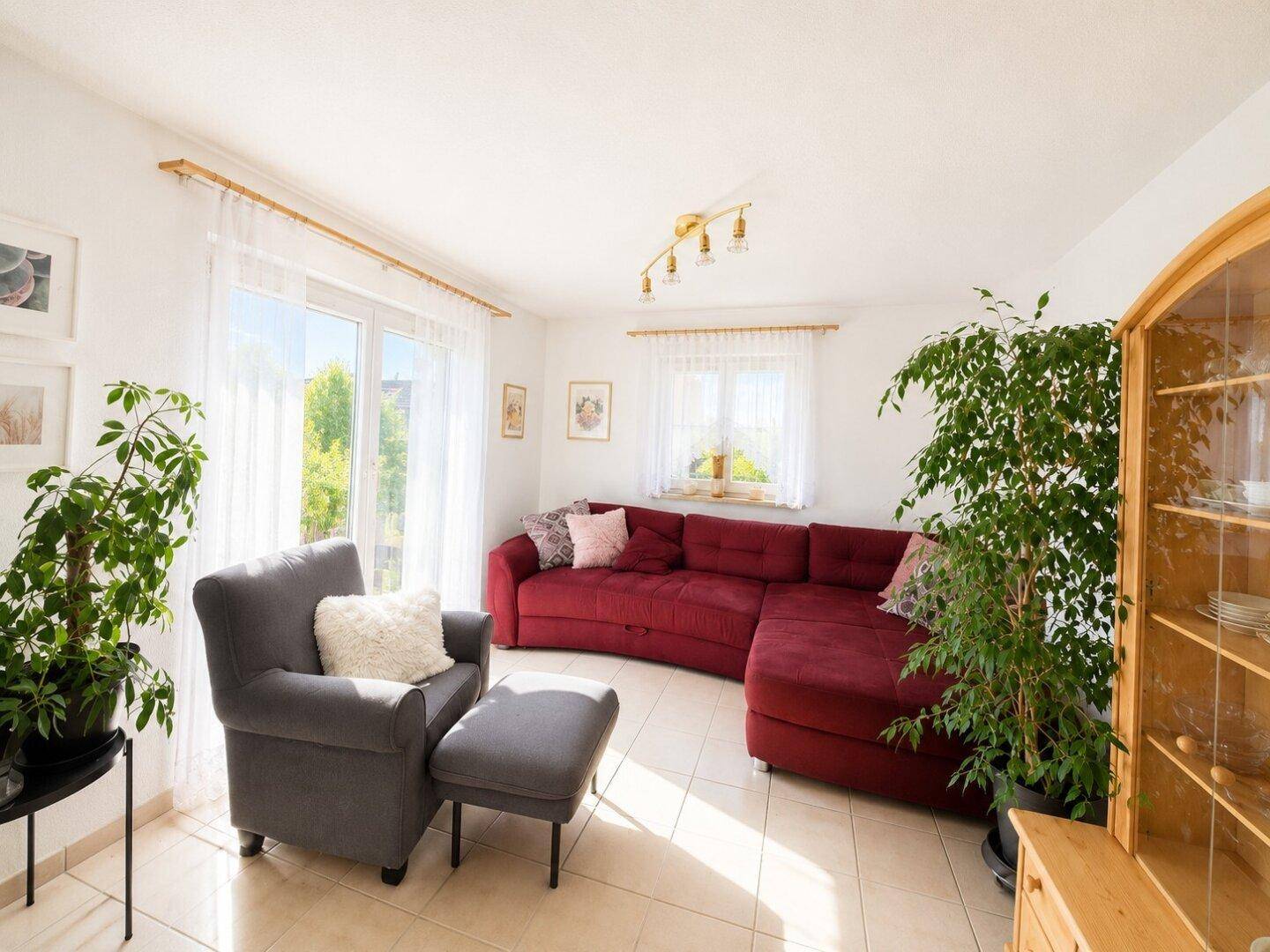 Helles Wohnzimmer mit rotem Ecksofa, bequemen Sesseln und großen Fenstern zum Garten.