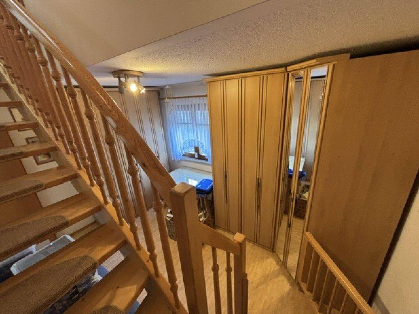 Holztreppe führt nach unten, umgeben von praktischen Einbauschränken aus Holz.
