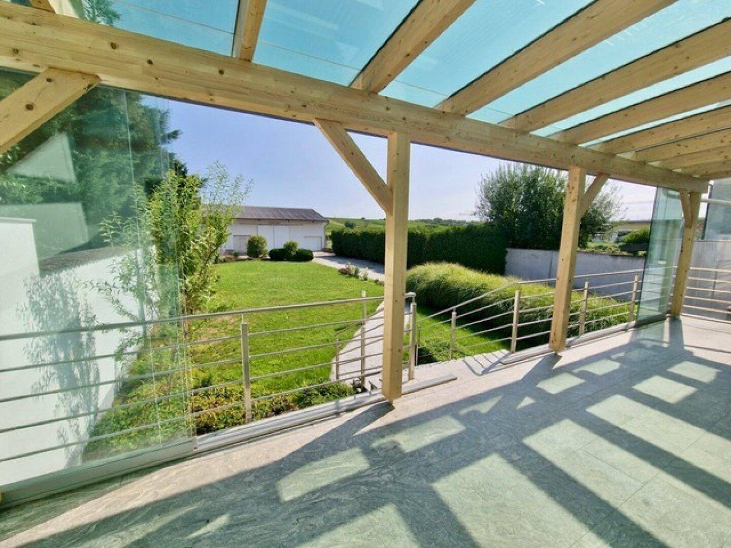 Überdachte Terrasse mit weitem Blick über den grünen Garten und die umliegende Landschaft.