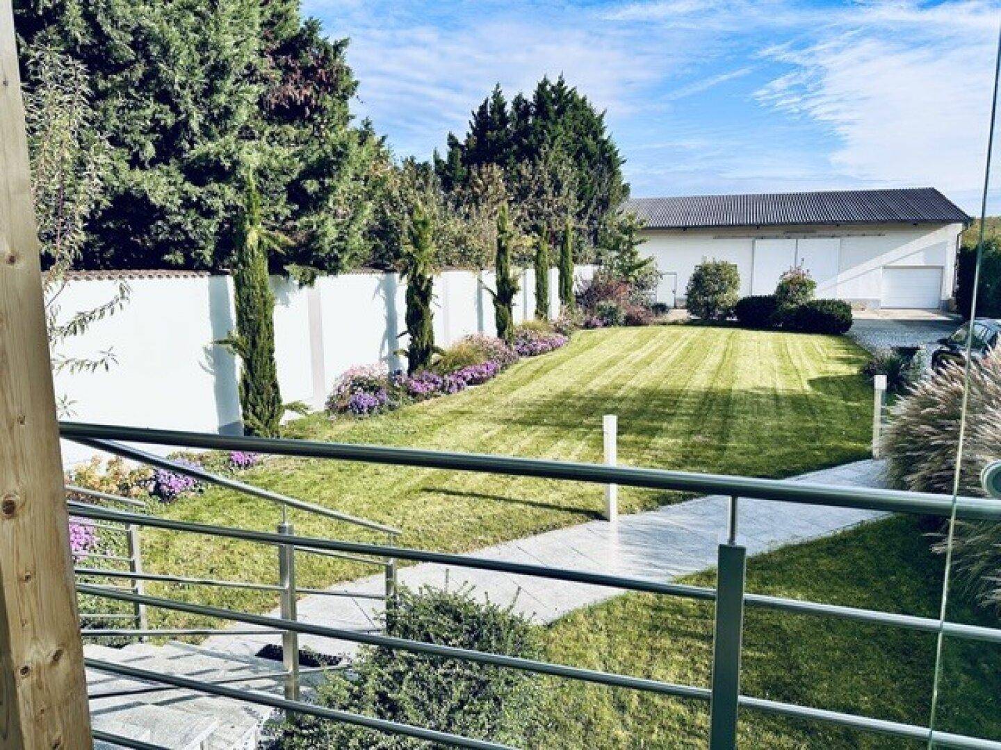 Weitläufiger Rasenbereich mit gepflegten Blumenbeeten und einer hohen Hecke, die das Grundstück begrenzt.