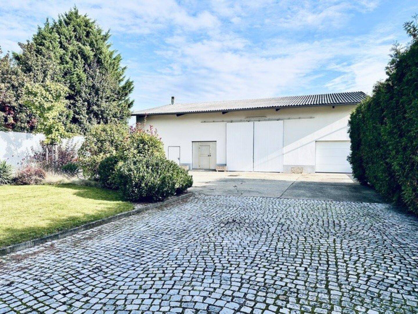 Großer gepflasterter Hofbereich vor einem weitläufigen Nebengebäude mit mehreren Toren und viel Platz.