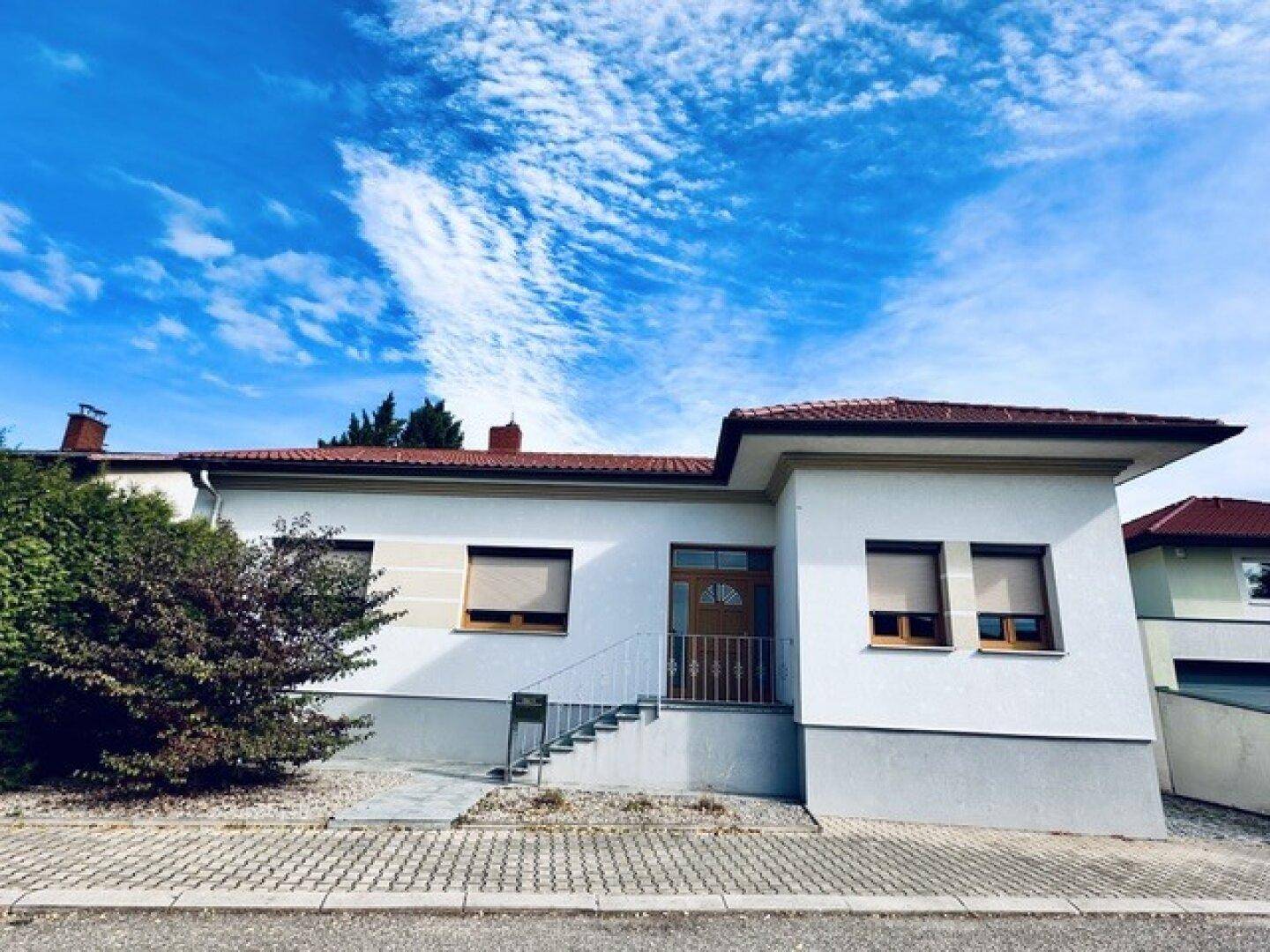 Vorderansicht des Einfamilienhauses mit Eingangsbereich, Treppe und gepflegter Fassade unter blauem Himmel.