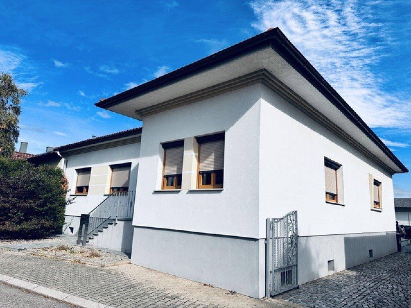 Seitenansicht des Hauses mit Rollläden an den Fenstern und einem kleinen Tor zum Grundstück.