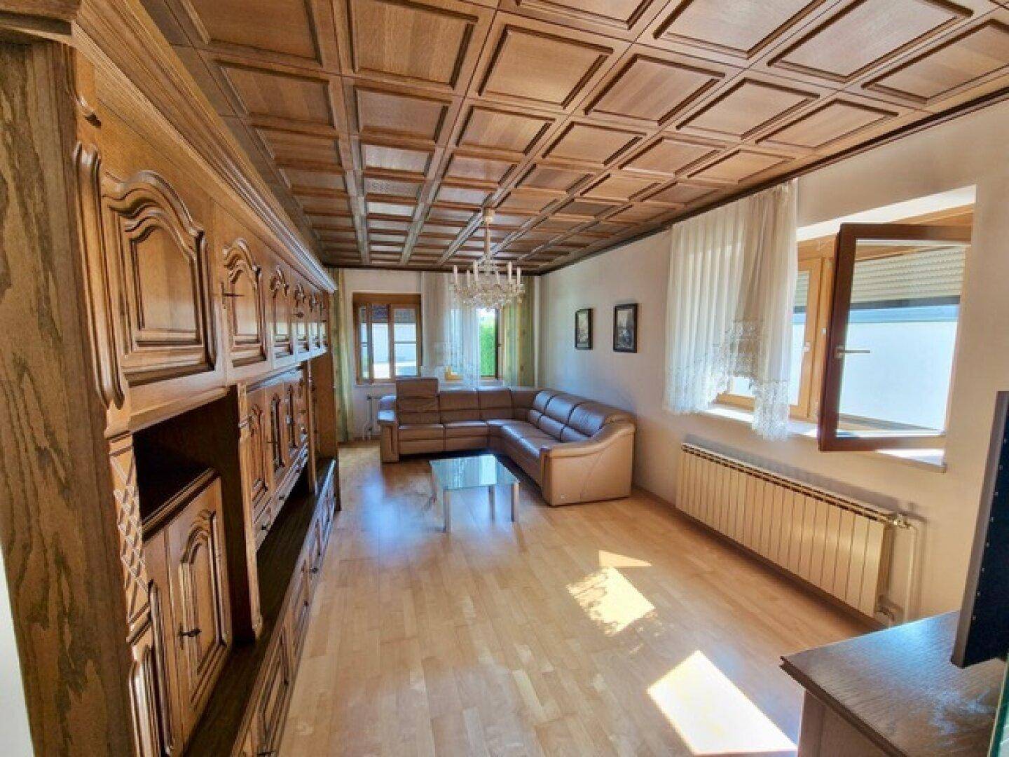 Geräumiges Wohnzimmer mit Holzkassettendecke, Parkettboden und bequemer Ledercouch.