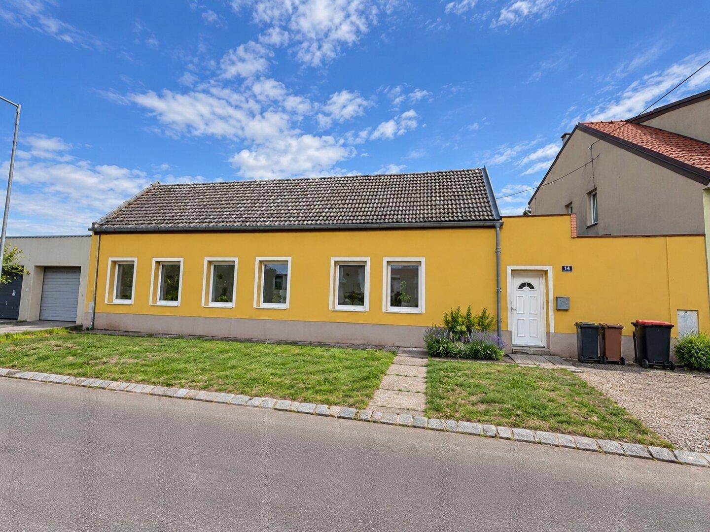 Gelbe Hausfassade von der Straße aus gesehen mit mehreren Fenstern und einem Eingangsbereich.