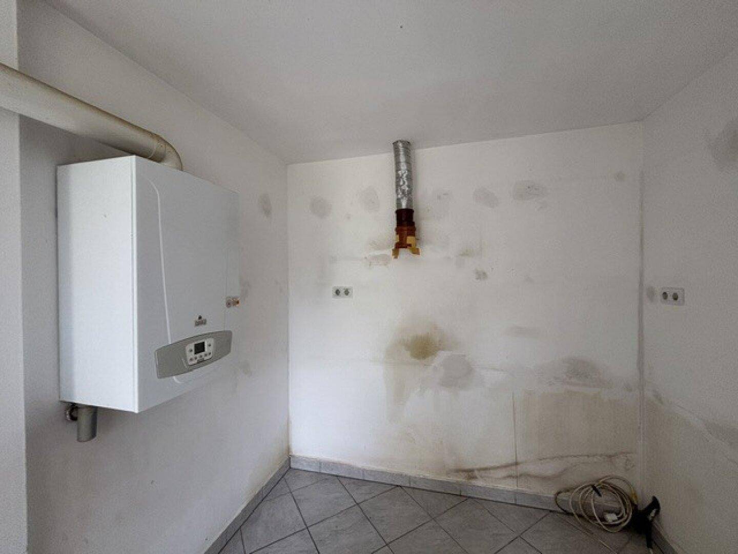 Einfacher Hauswirtschaftsraum mit Heizkessel und sichtbaren Gebrauchsspuren an den Wänden.