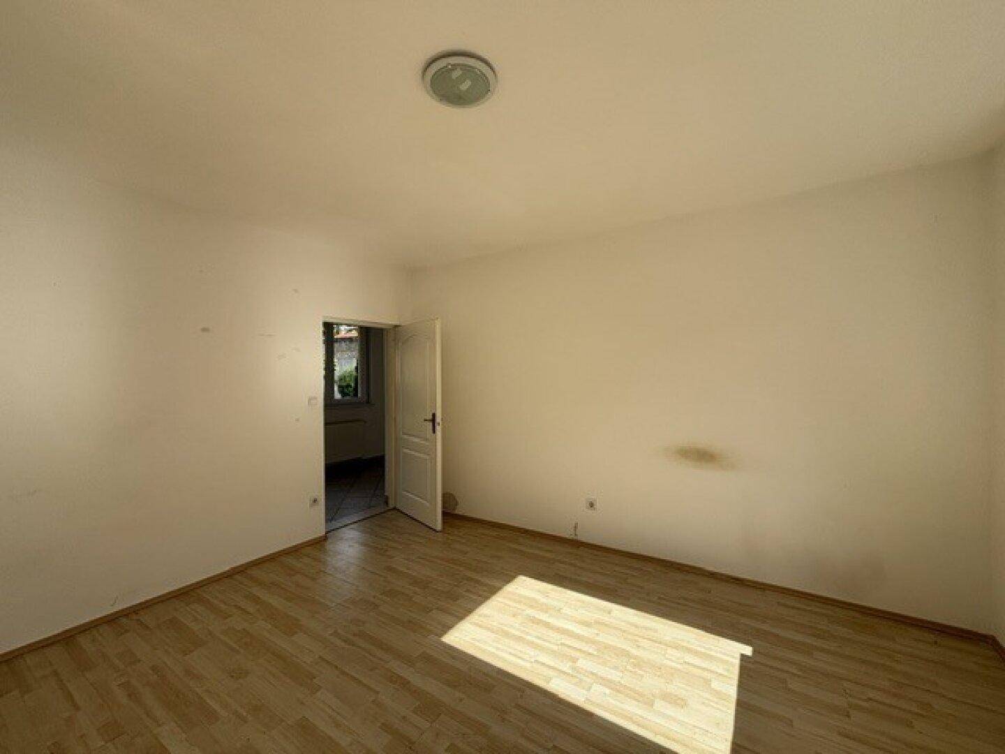 Leeres Schlafzimmer mit Laminatboden und einer Tür, die zu einem weiteren Raum führt.