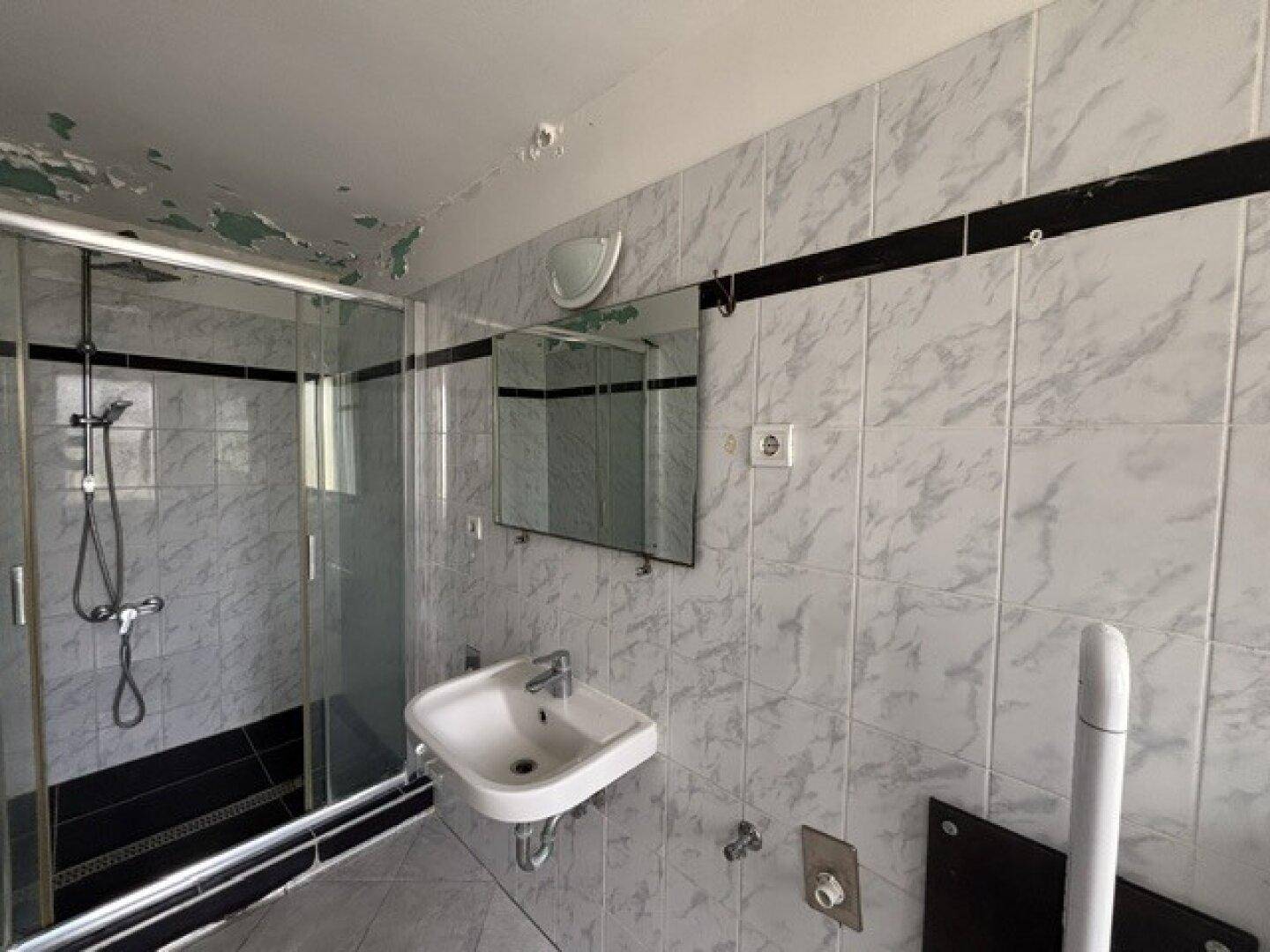 Badezimmer mit Duschkabine, Einzelwaschbecken und gefliesten Wänden im Stil der 80er Jahre.