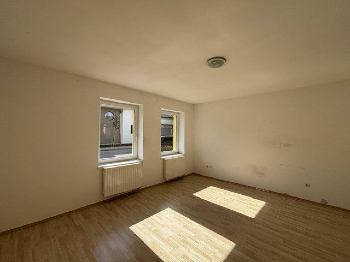 Leeres Schlafzimmer mit Laminatboden, zwei Fenstern und viel natürlichem Tageslicht.