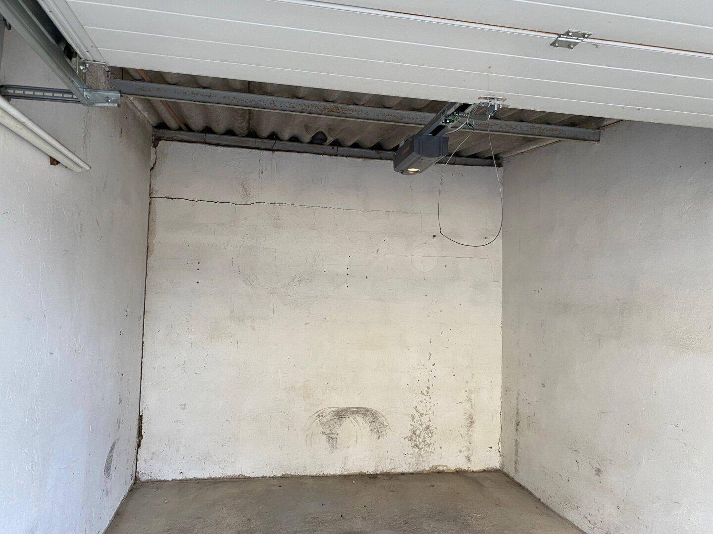 Leere Garage mit Betonboden und automatischem Garagentoröffner an der Decke.
