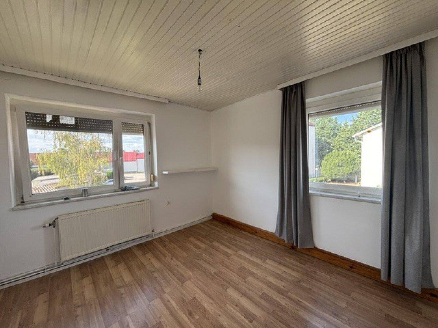 Helles Schlafzimmer mit zwei Fenstern, Heizkörper und Laminatboden, bietet viel Tageslicht.