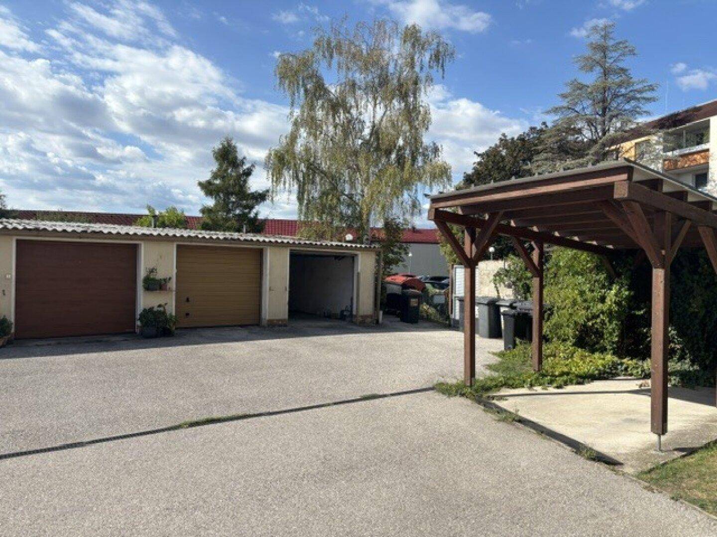 Mehrere Garagen und ein Carport auf einem asphaltierten Hof unter blauem Himmel.