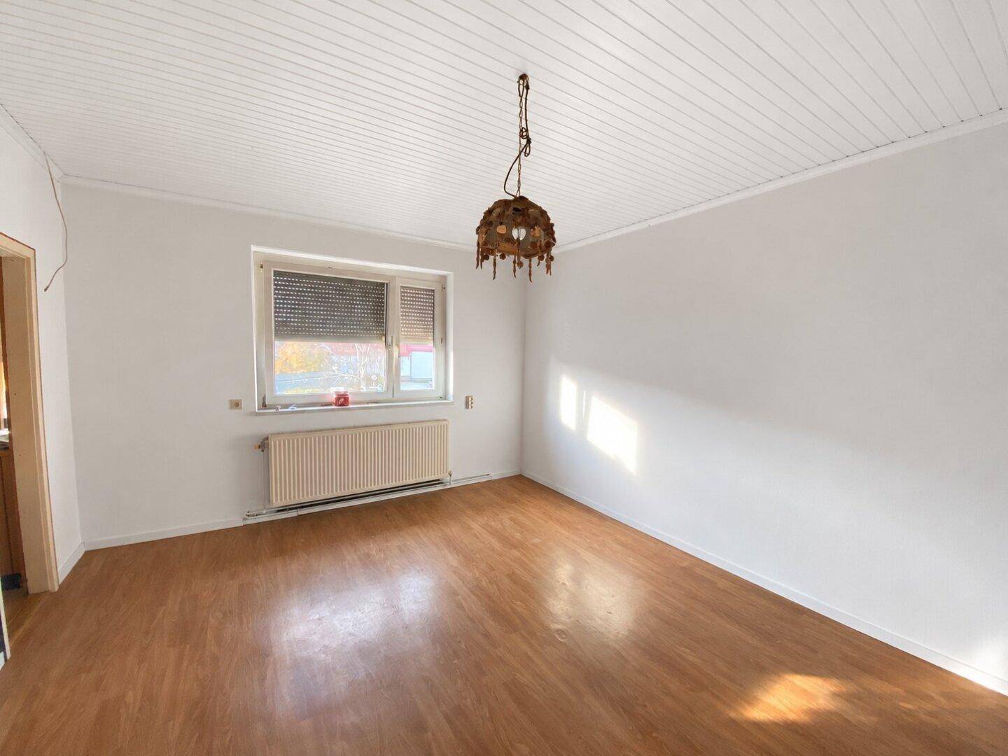 Geräumiges Zimmer mit Laminatboden, weiß gestrichenen Wänden und einem Fenster mit Rollladen.