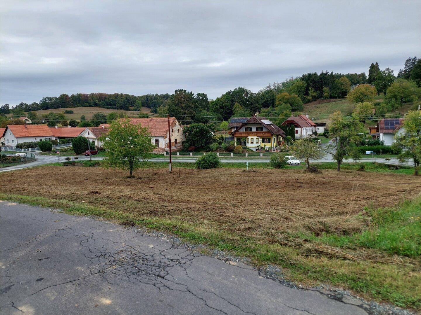 Großes Grundstück in idyllischer Hügellandschaft, umgeben von Wohnhäusern und viel Grün.