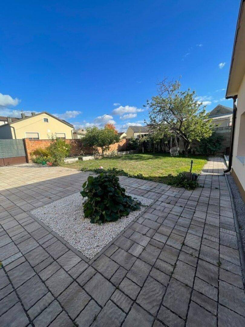 Sonniger Gartenbereich mit gepflasterter Terrasse und Rasenfläche, umgeben von Häusern.