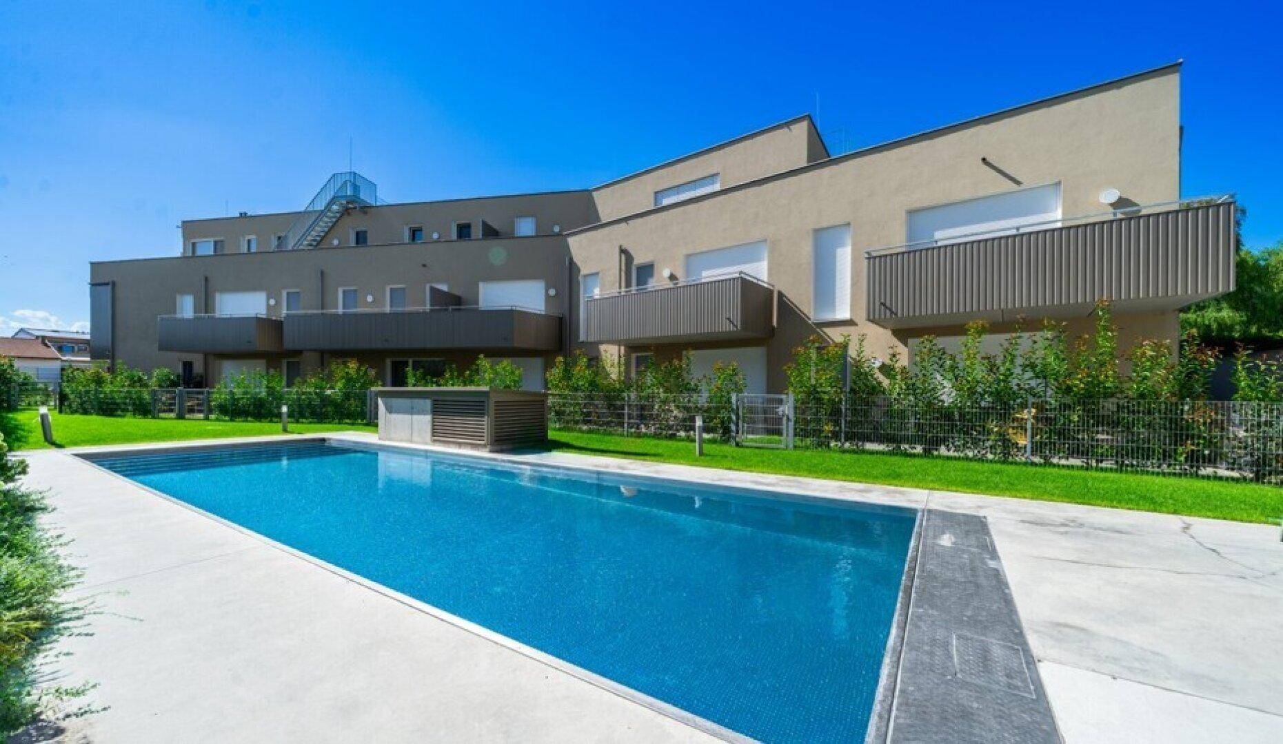 Moderne Wohnanlage mit Gemeinschaftspool und gepflegter Grünfläche unter strahlend blauem Himmel.