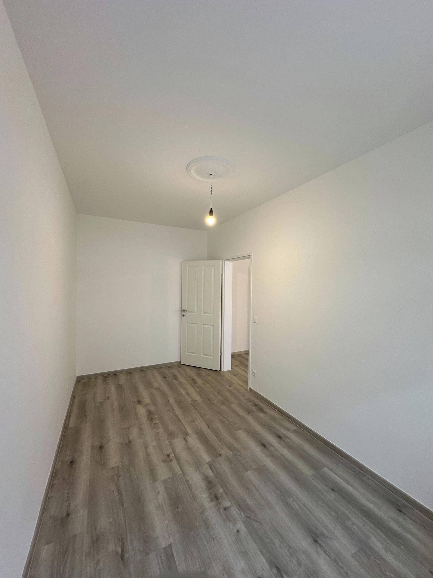 Leeres Zimmer mit Laminatboden und zwei Türen, bietet Zugang zu angrenzenden Bereichen.