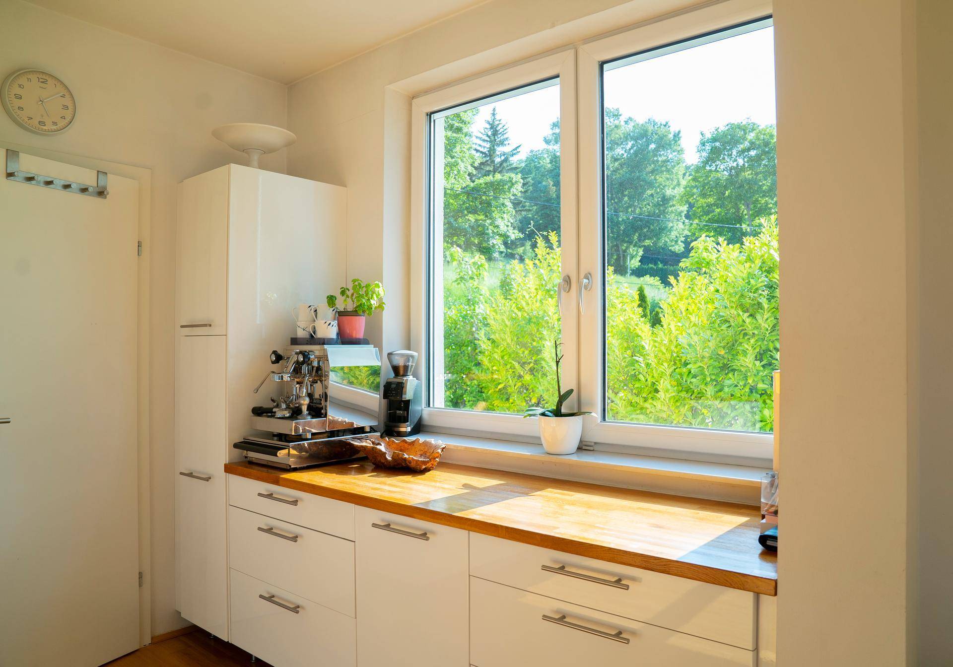 Moderne Küche mit weißen Schränken, Holz-Arbeitsplatte und großem Fenster mit Blick ins Grüne.