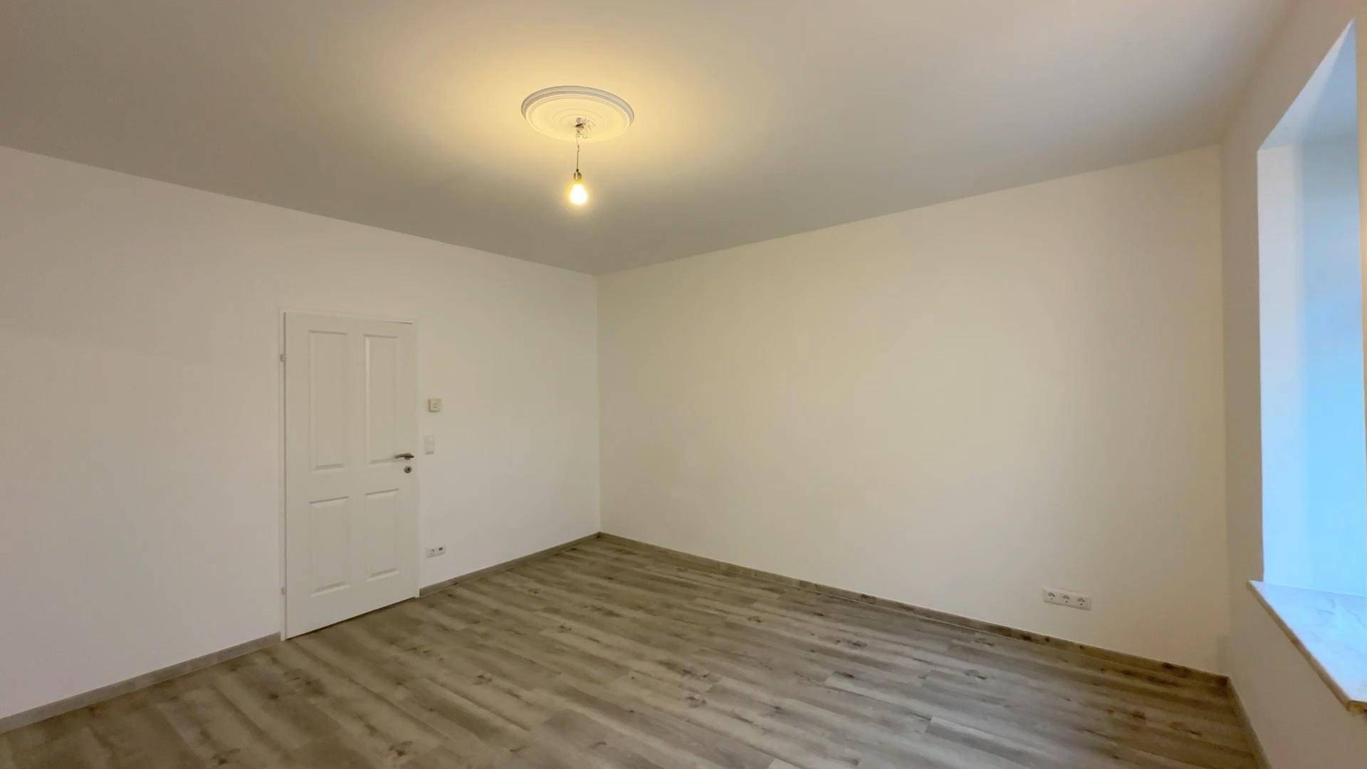 Leeres Zimmer mit Laminatboden und weißer Tür, bereit für individuelle Einrichtung.