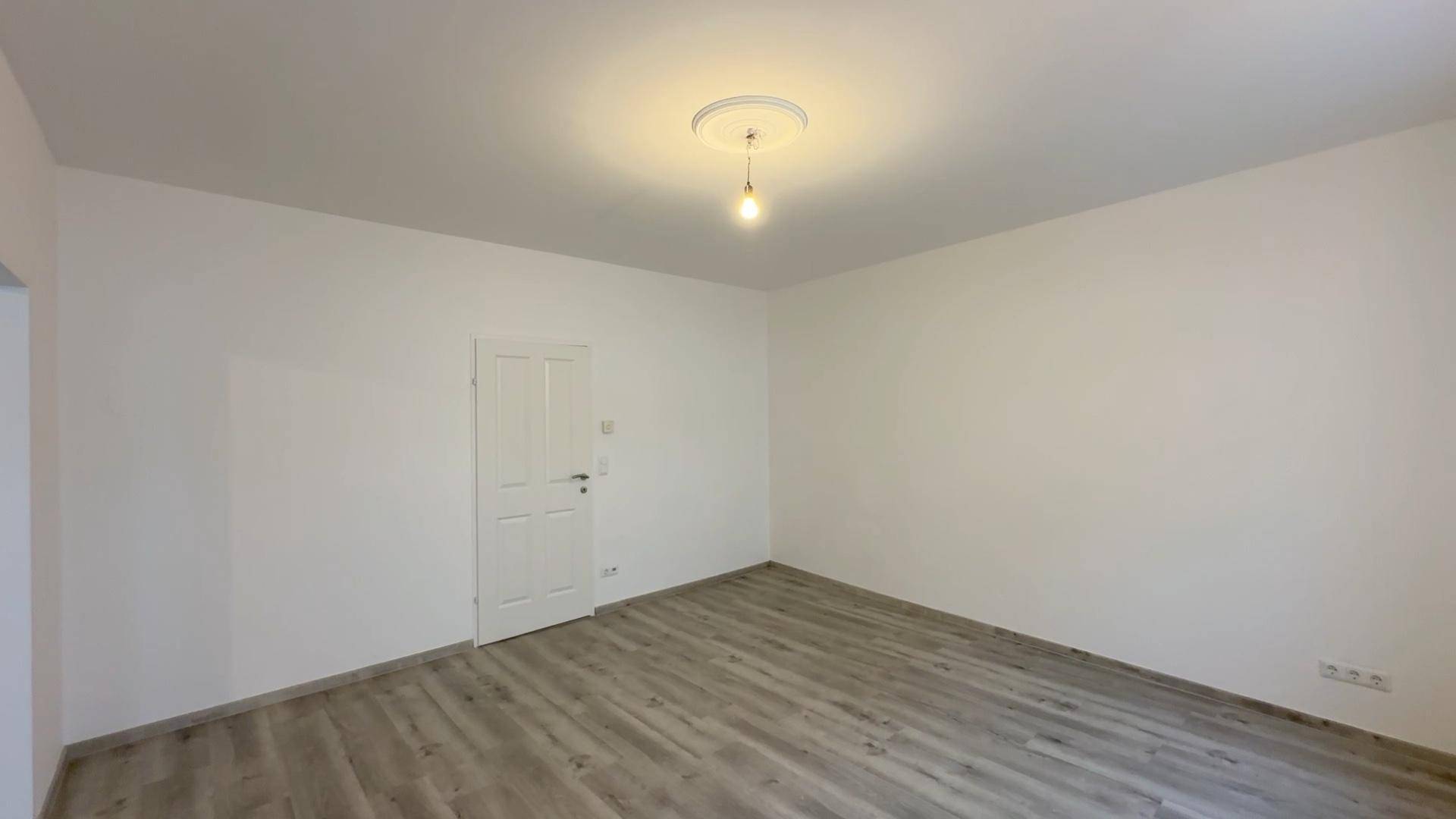 Leeres Zimmer mit Laminatboden und weißer Tür, bietet vielseitige Nutzungsmöglichkeiten.
