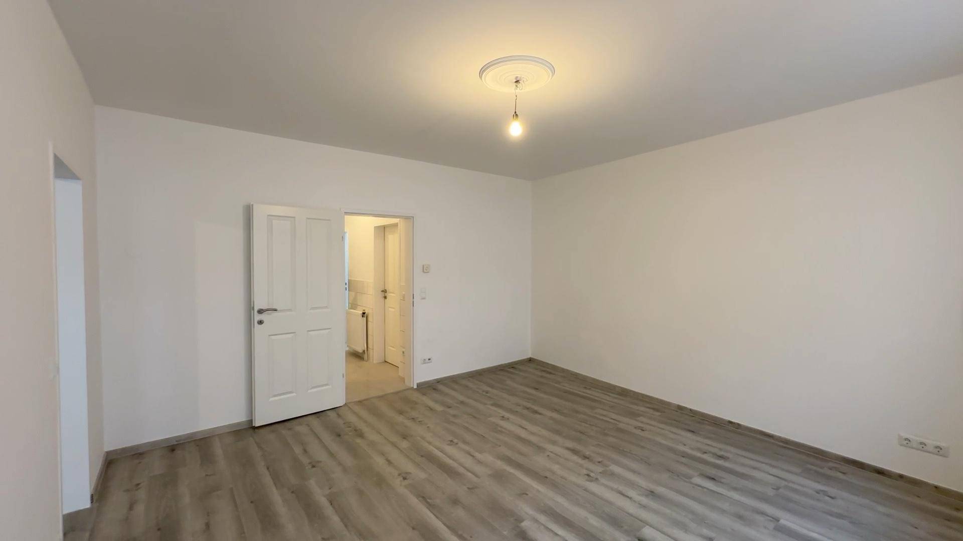 Geräumiges Zimmer mit Laminatboden und offener Tür zu einem angrenzenden Bereich.
