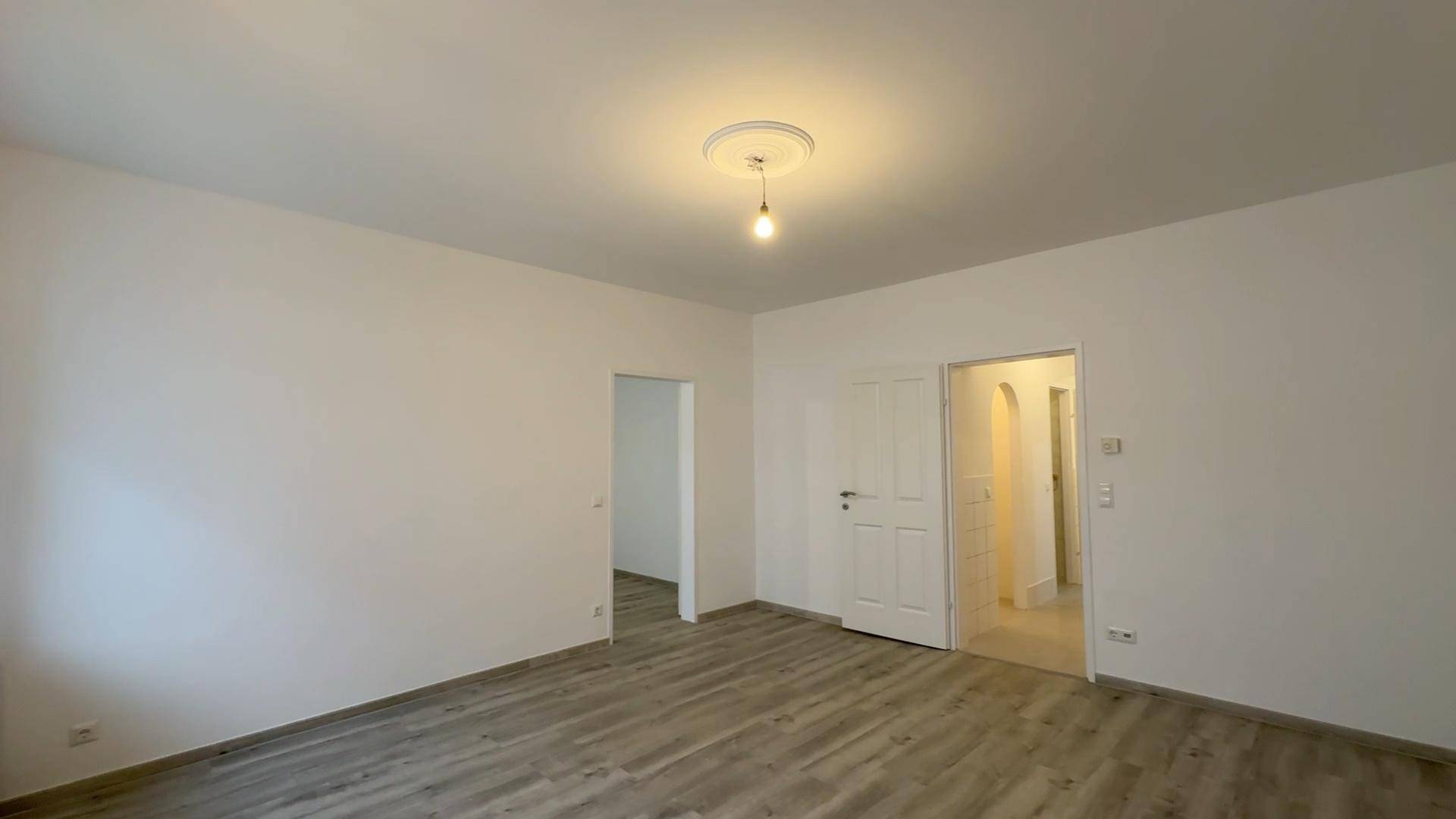 Helles Zimmer mit Laminatboden und zwei offenen Türen, verbindet mehrere Wohnbereiche.