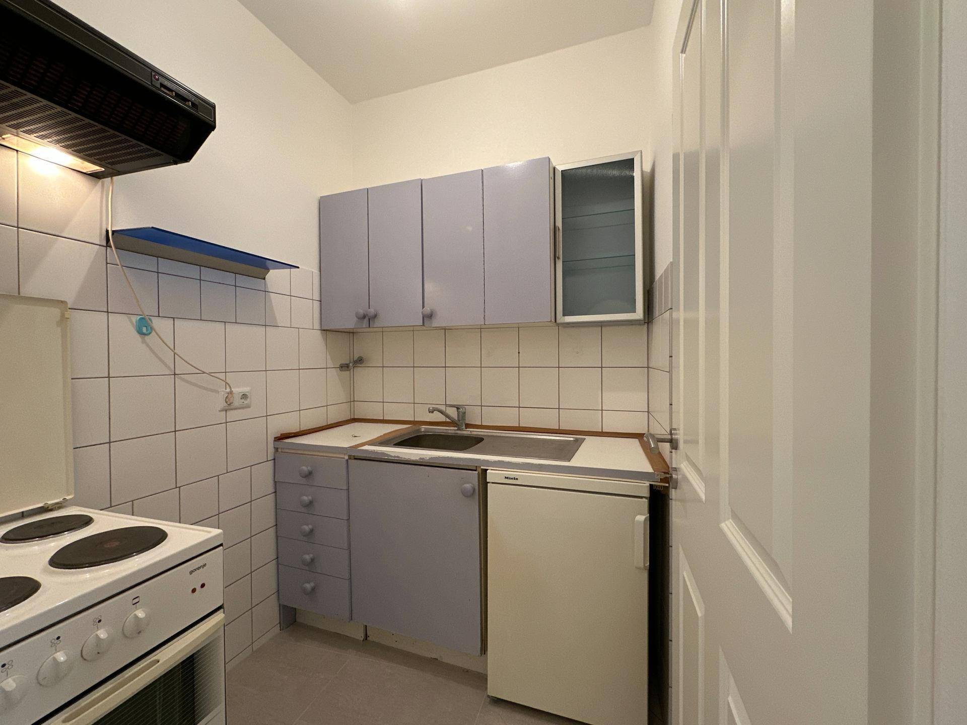 Funktionale kleine Küche mit hellblauen Schränken, Herd und Kühlschrank, gefliestem Spritzschutz.