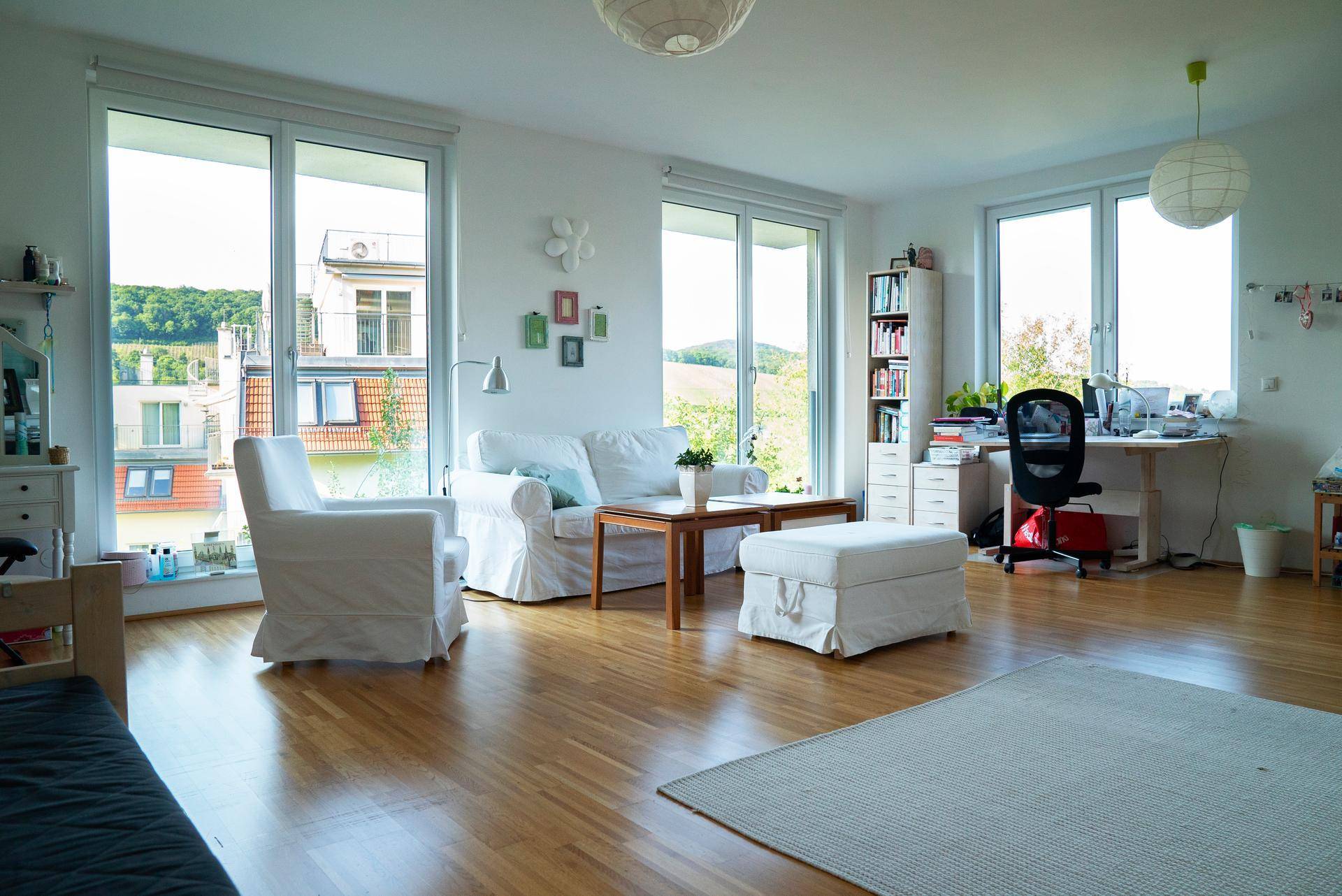 Geräumiger Wohnbereich mit weißen Sofas, Holzboden und großen Fenstern mit Blick ins Grüne.