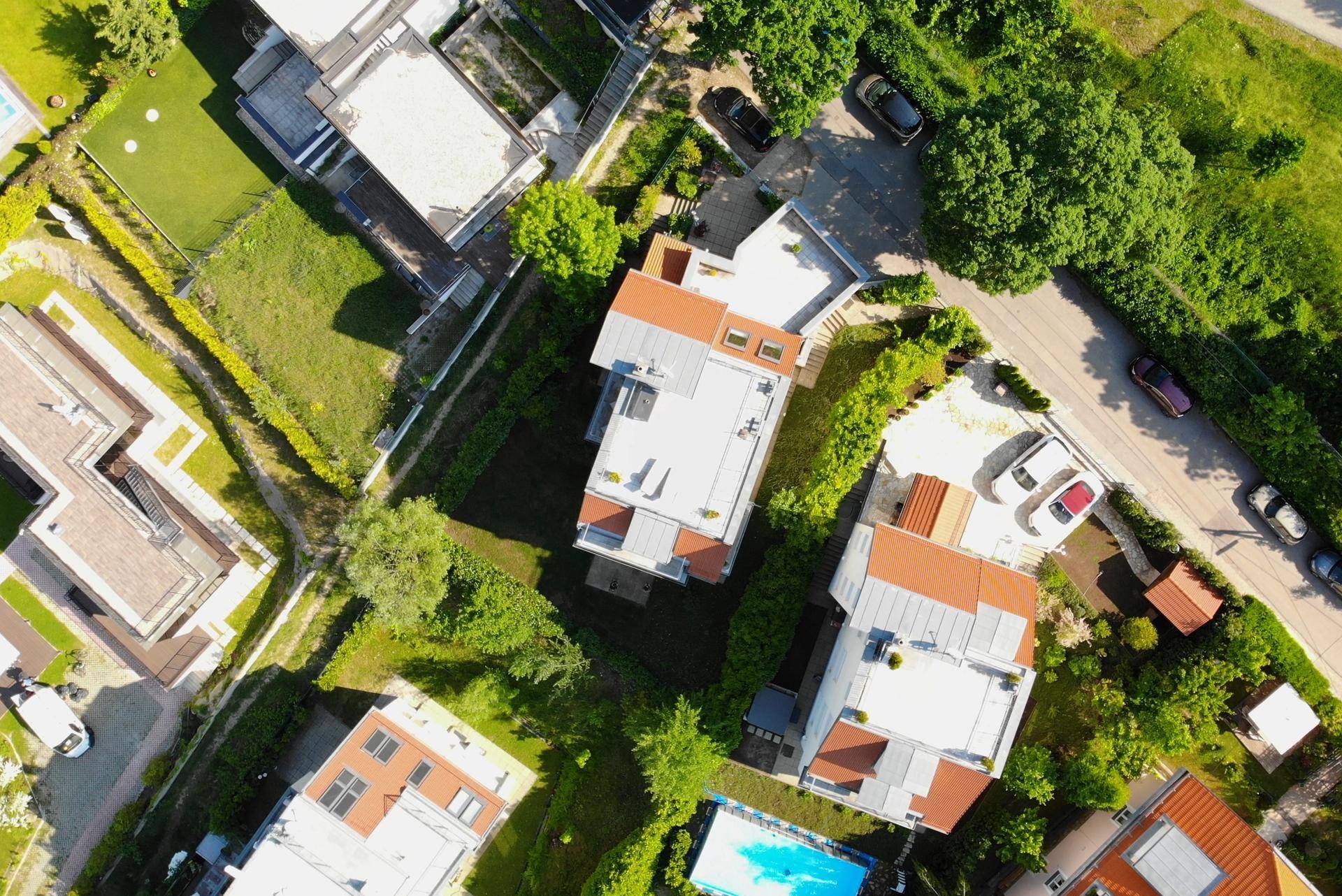 Luftaufnahme einer Wohnsiedlung mit mehreren Gebäuden, Gärten und einem Pool in grüner Umgebung.