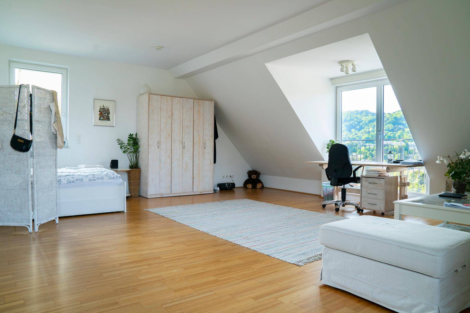 Geräumiges Schlafzimmer im Dachgeschoss mit Holzboden, Schrank und Arbeitsbereich mit Weitblick.