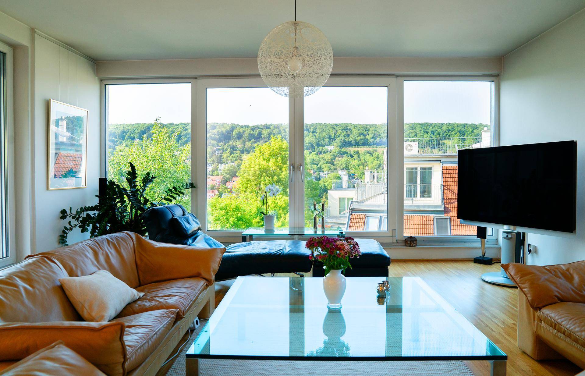 Helles Wohnzimmer mit Ledersofas, Glascouchtisch und großen Fenstern mit Panoramablick ins Grüne.