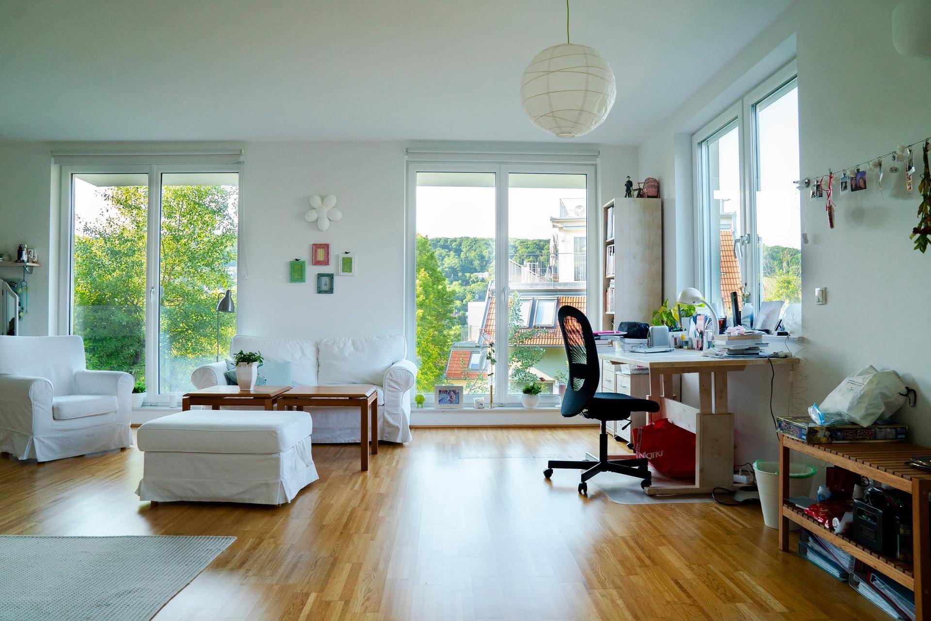 Lichtdurchflutetes Wohnzimmer mit Arbeitsbereich, weißen Möbeln und Panoramablick ins Grüne.