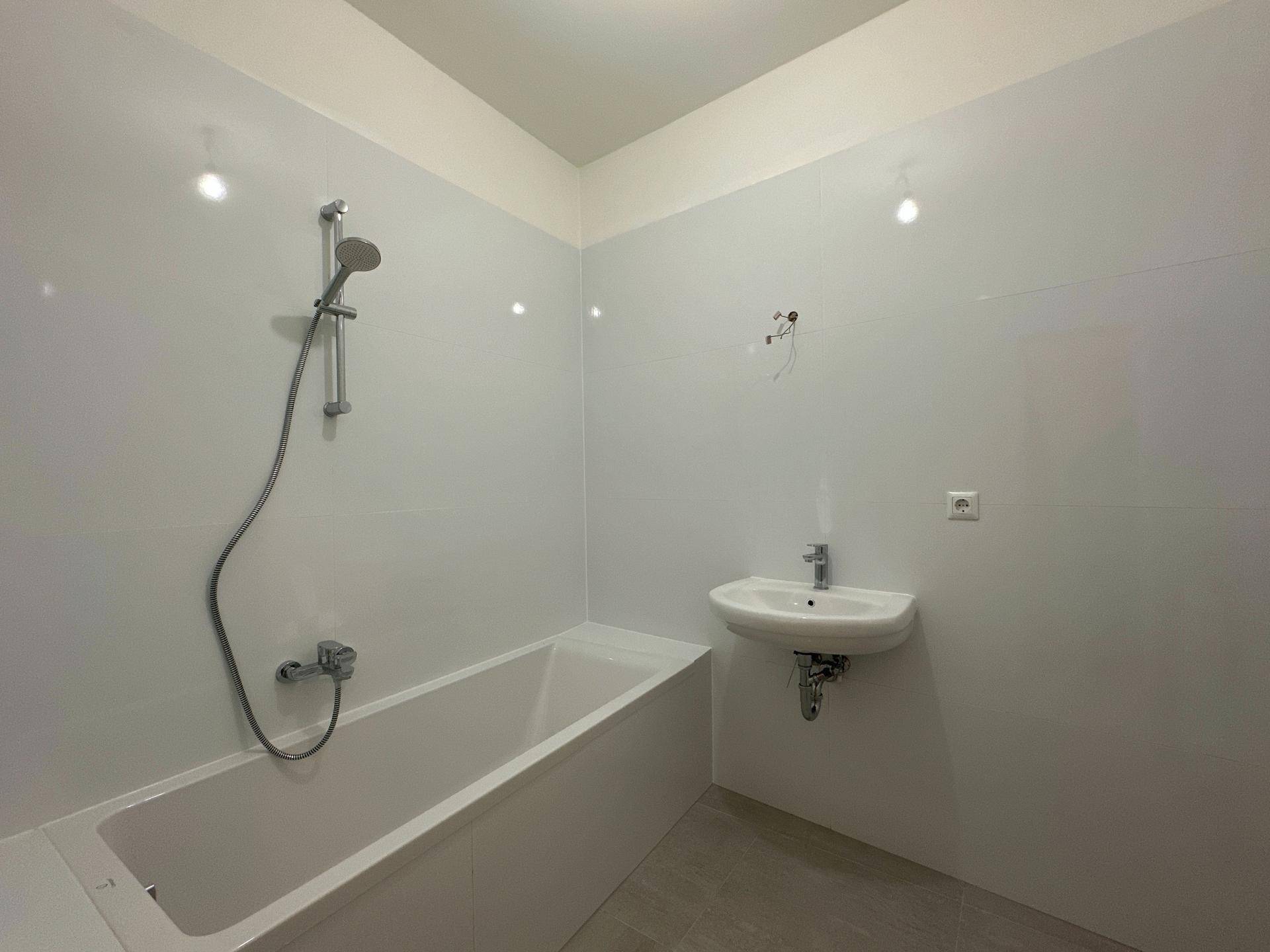 Modern gefliestes Badezimmer mit Badewanne, Duscharmatur und Einzelwaschbecken.