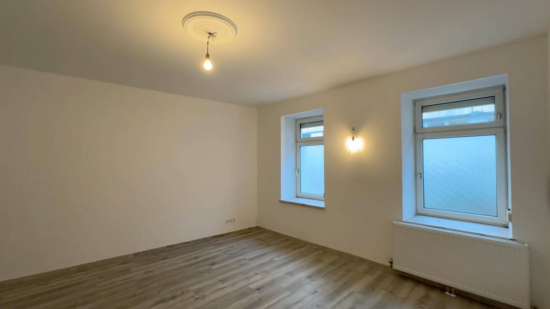 Helles, geräumiges Zimmer mit Laminatboden und zwei Fenstern, bietet viel Tageslicht.