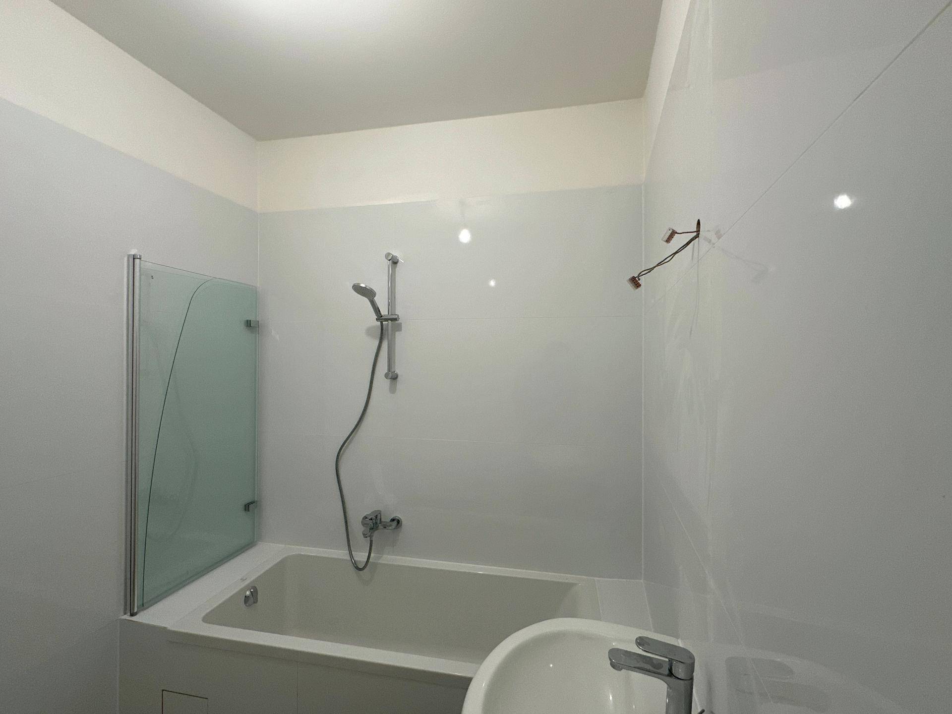 Helles Badezimmer mit Badewanne, Duschabtrennung aus Glas und Einzelwaschbecken.