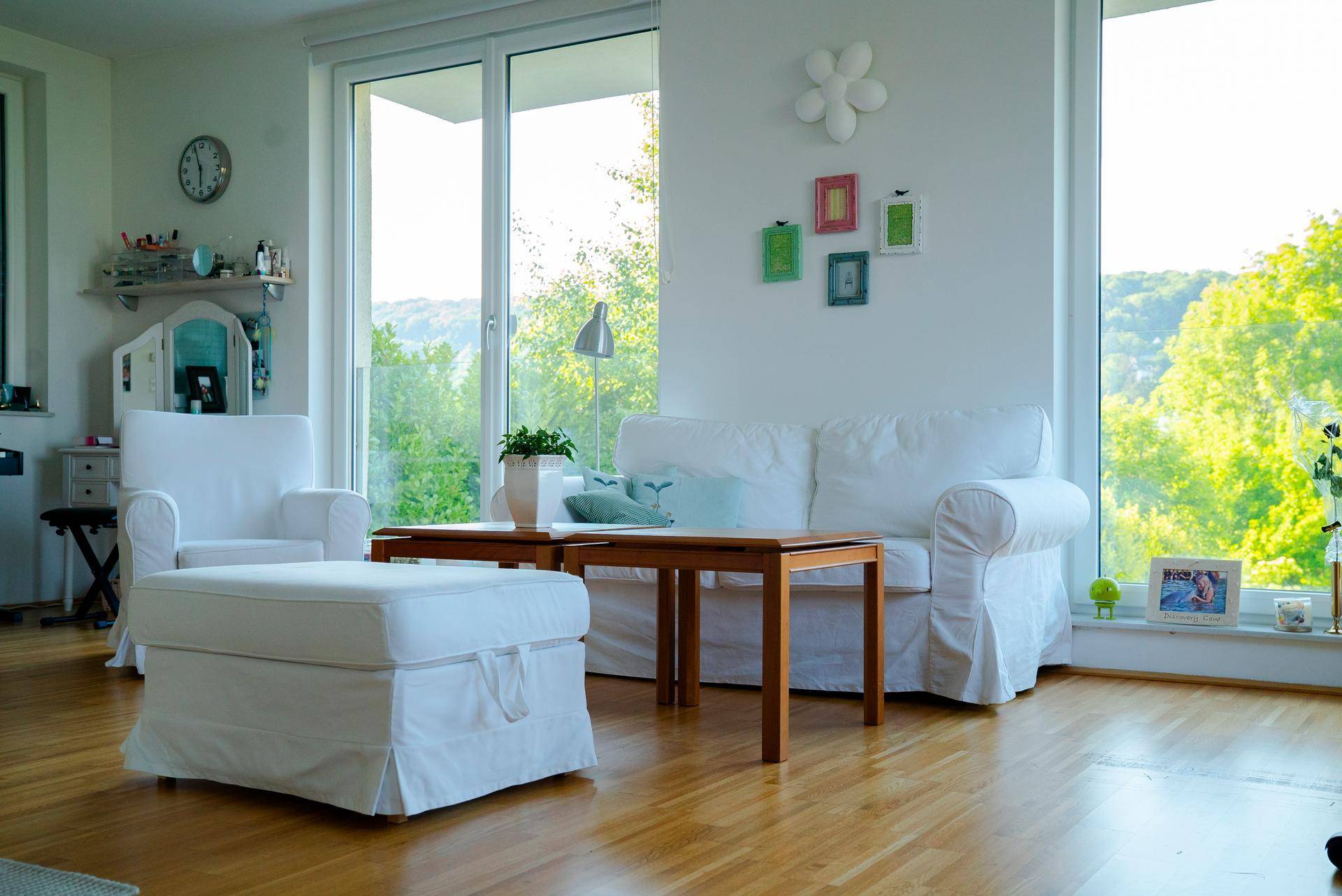 Gemütlicher Wohnbereich mit weißen Sofas, Holztisch und großen Fenstern mit Blick ins Grüne.
