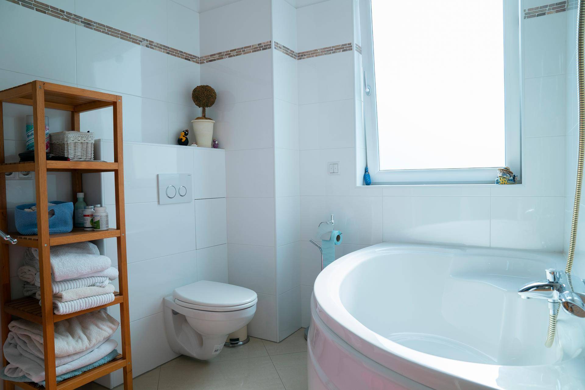 Helles Badezimmer mit Eckbadewanne, Wand-WC und Holzregal für Handtücher.