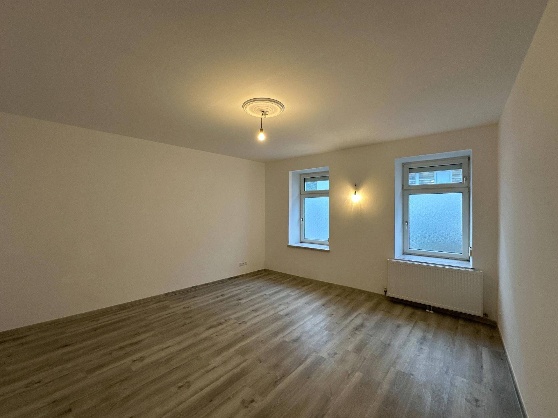 Großzügiges Zimmer mit Laminatboden und zwei Fenstern, ideal für helle Wohnraumgestaltung.