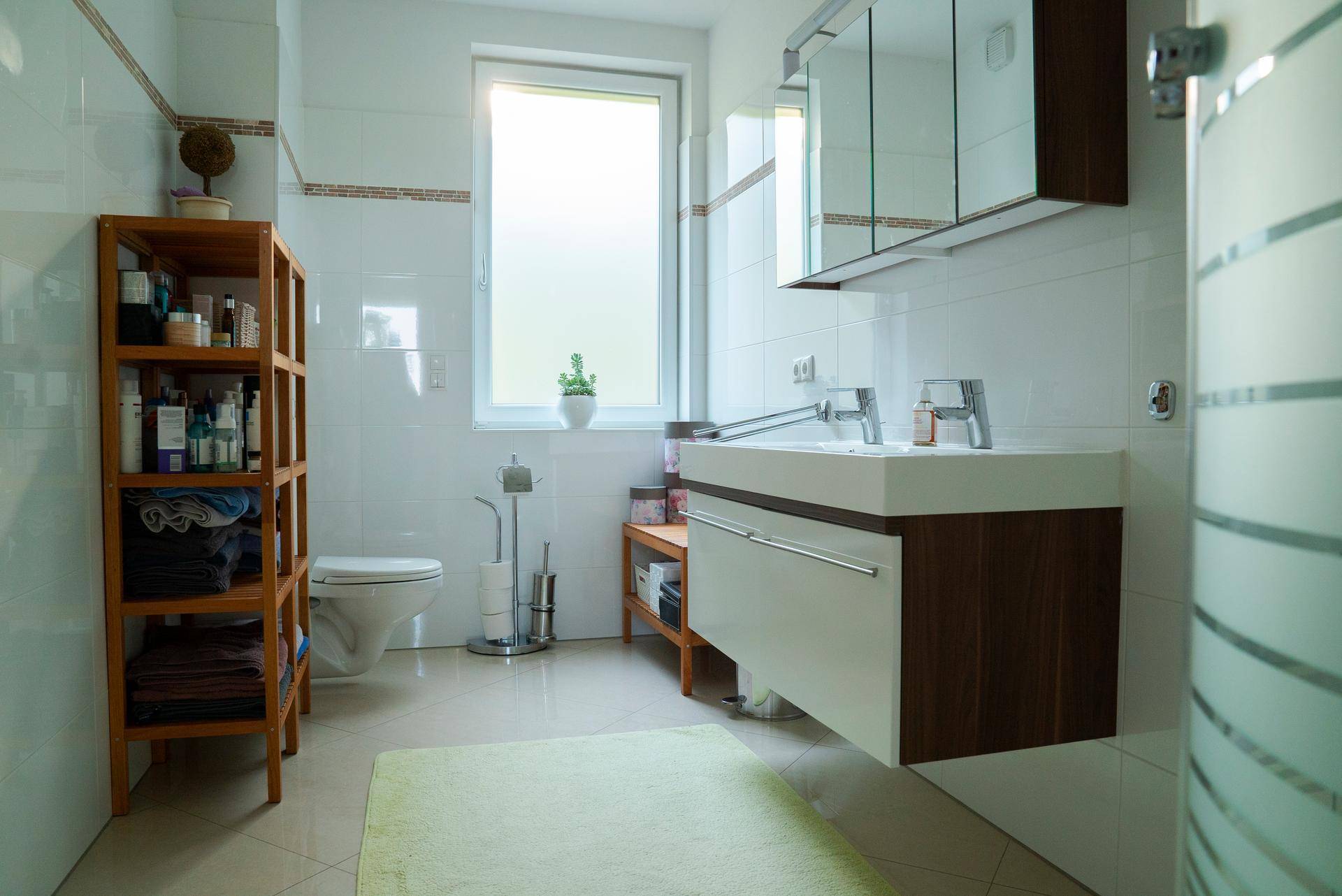Helles Badezimmer mit Fenster, modernem Waschtisch, Toilette und praktischen Holzregalen.