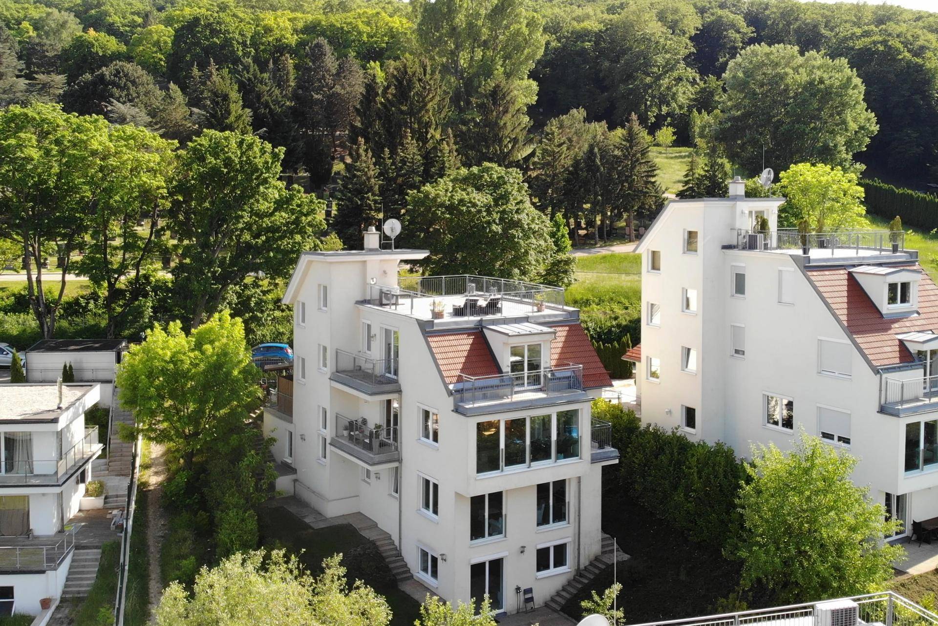 Modernes Wohngebäude mit mehreren Balkonen und einer Dachterrasse, umgeben von viel Grün.