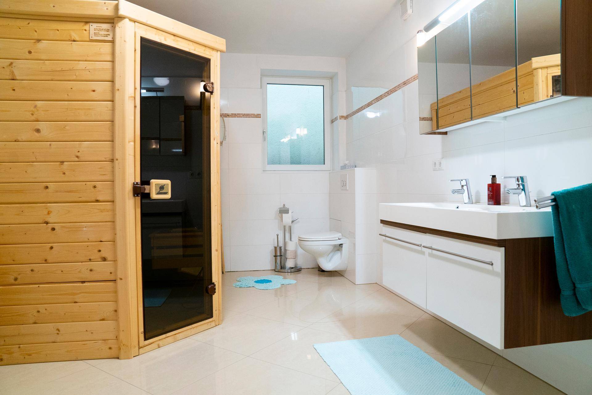 Badezimmer mit integrierter Sauna, Doppelwaschbecken und großem Fenster für Tageslicht.