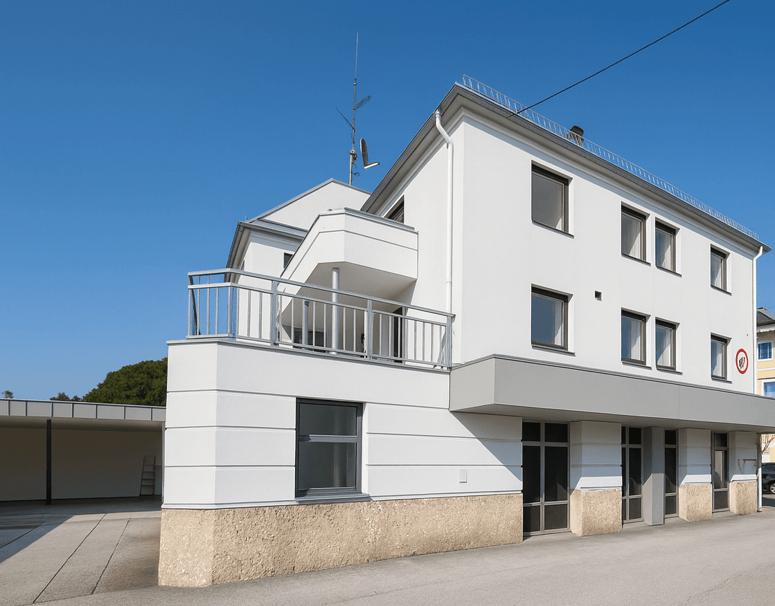 Moderne weiße Fassade des Gebäudes mit Balkon und angrenzendem Carportbereich.