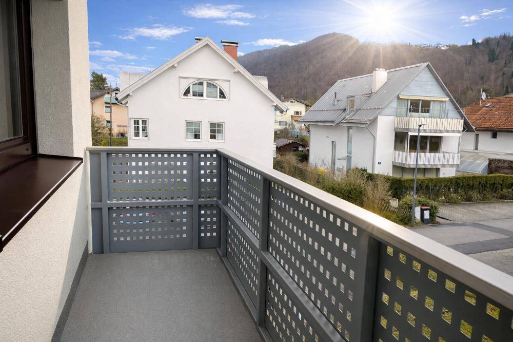 Kleiner Balkon mit modernem Gittergeländer und Blick auf die umliegenden Häuser und Berge.
