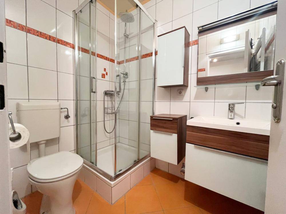 Badezimmer mit Duschkabine, WC, Waschbecken und hellen Fliesen mit orangefarbenen Akzenten für Frische.
