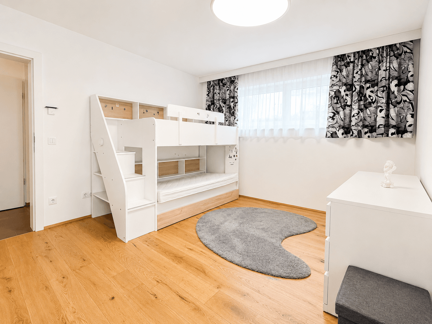 Kinderzimmer mit modernem Etagenbett, hellem Holzboden und großem Fenster für natürliche Beleuchtung.