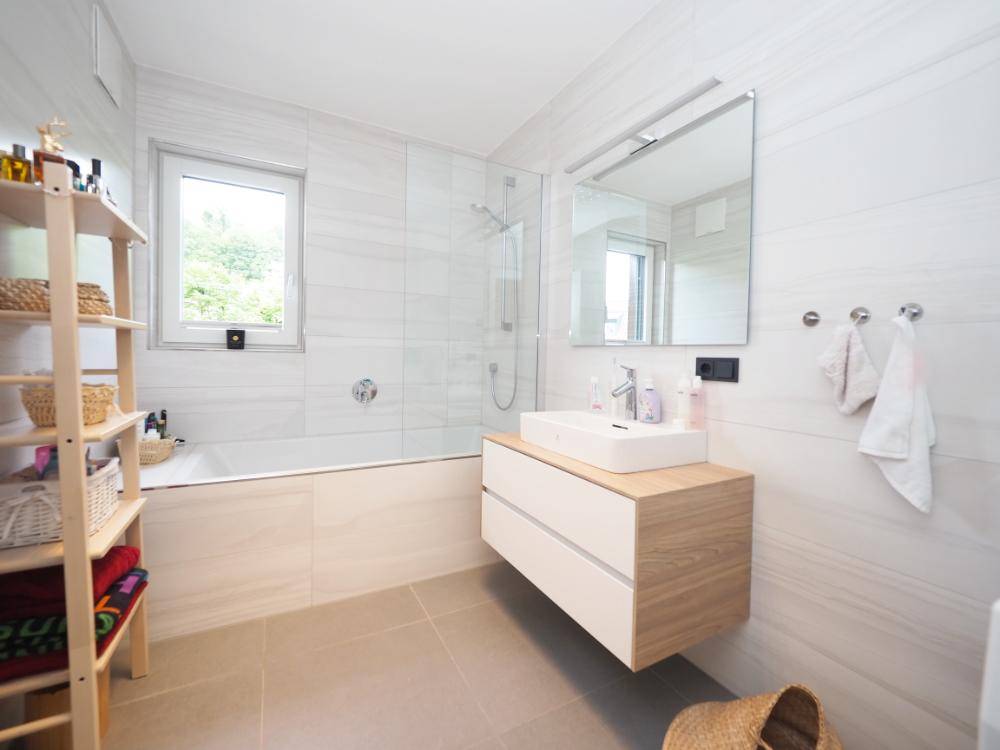 Modernes Badezimmer mit Badewanne, Dusche, schwebendem Waschtisch und Fenster.