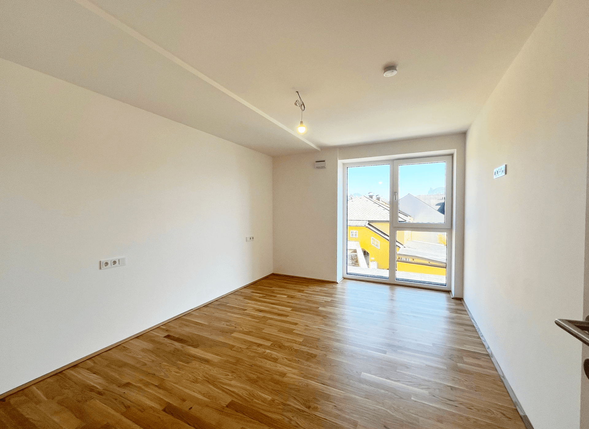Leeres Schlafzimmer mit hellem Holzboden und einem großen Fenster mit Blick auf die Umgebung.